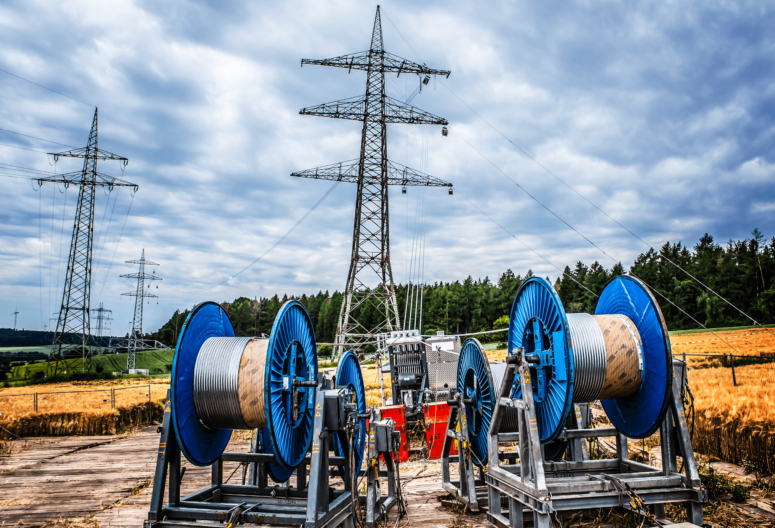 Drum stands with conductor drums on an overhead line site, transmission towers behind