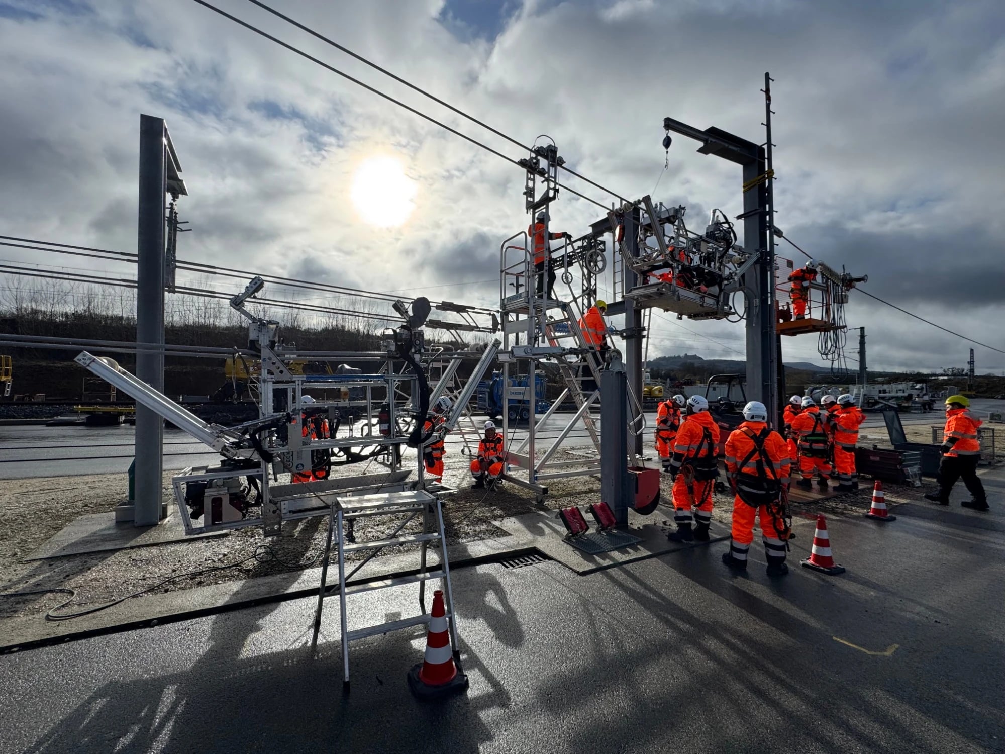 Trainees in orange high-visibility workwear during hands-on training on overhead contact line equipment