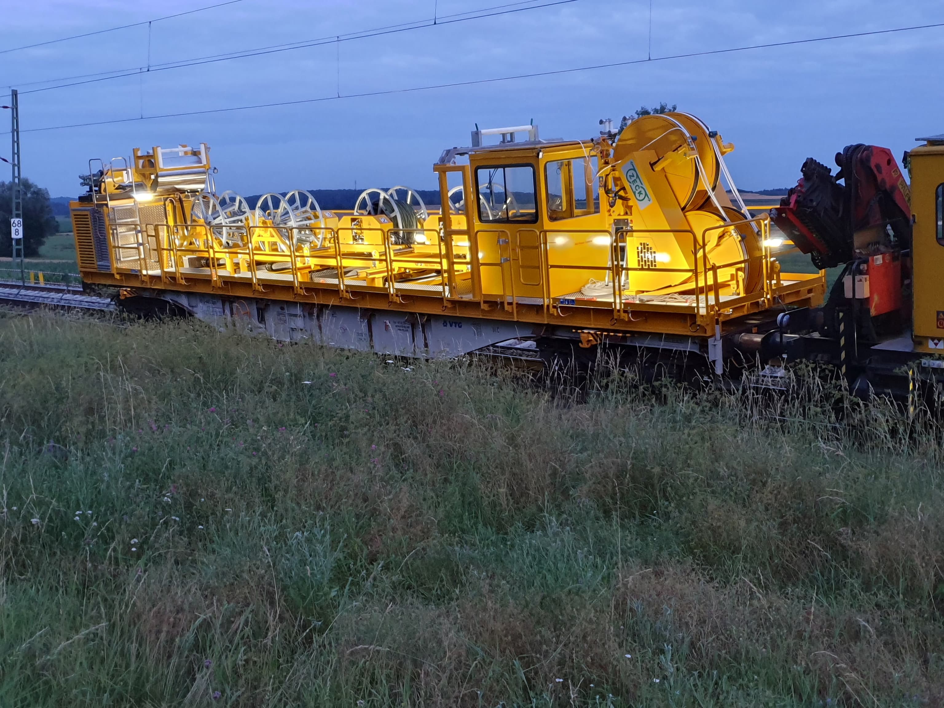 Gelbe ZECK-Fahrdraht-Verlegeeinheit BM 984 auf einem Bahnwagen in der Abenddämmerung