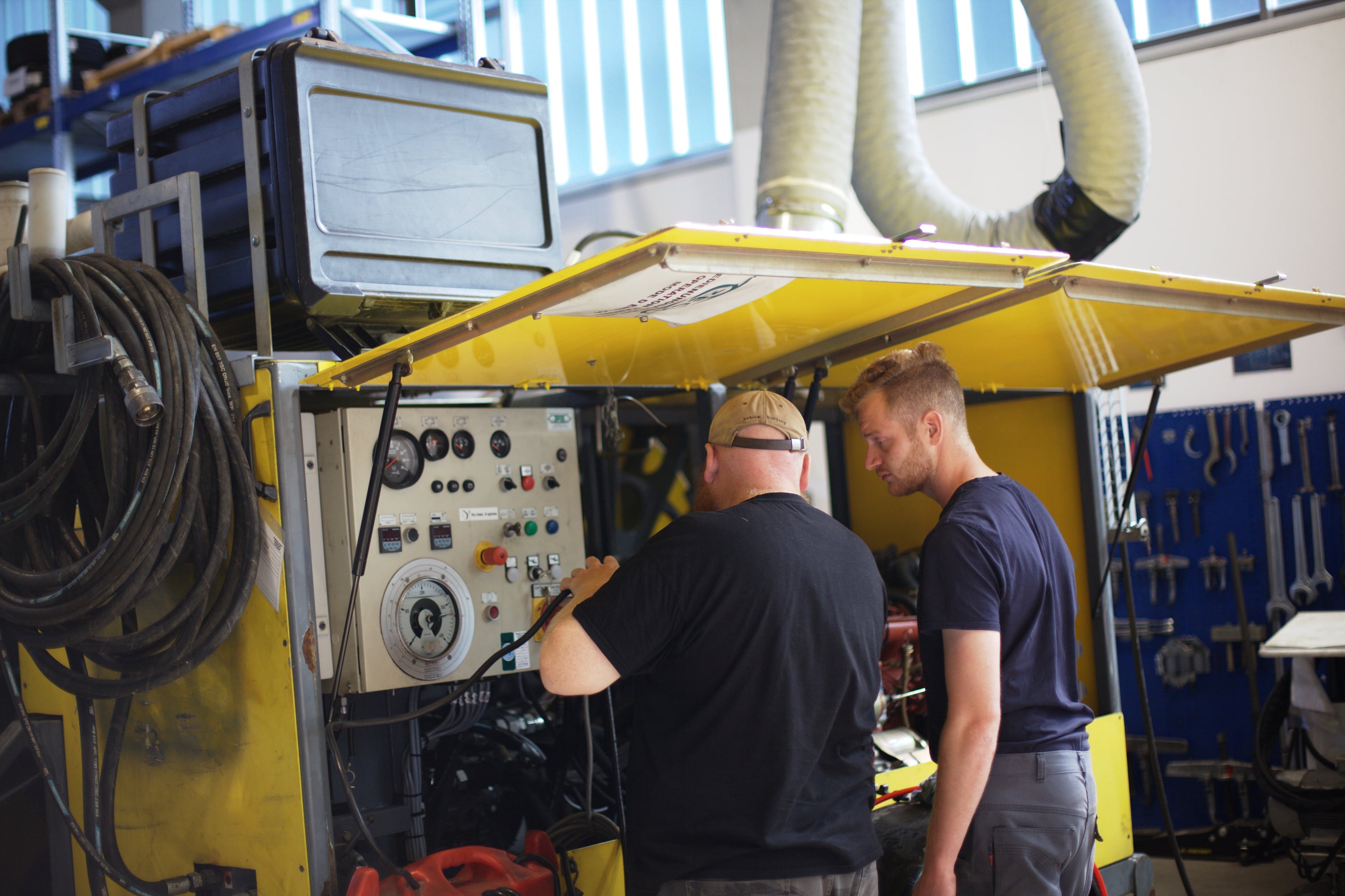 Two ZECK service technicians checking the control panel of a yellow machine in the workshop