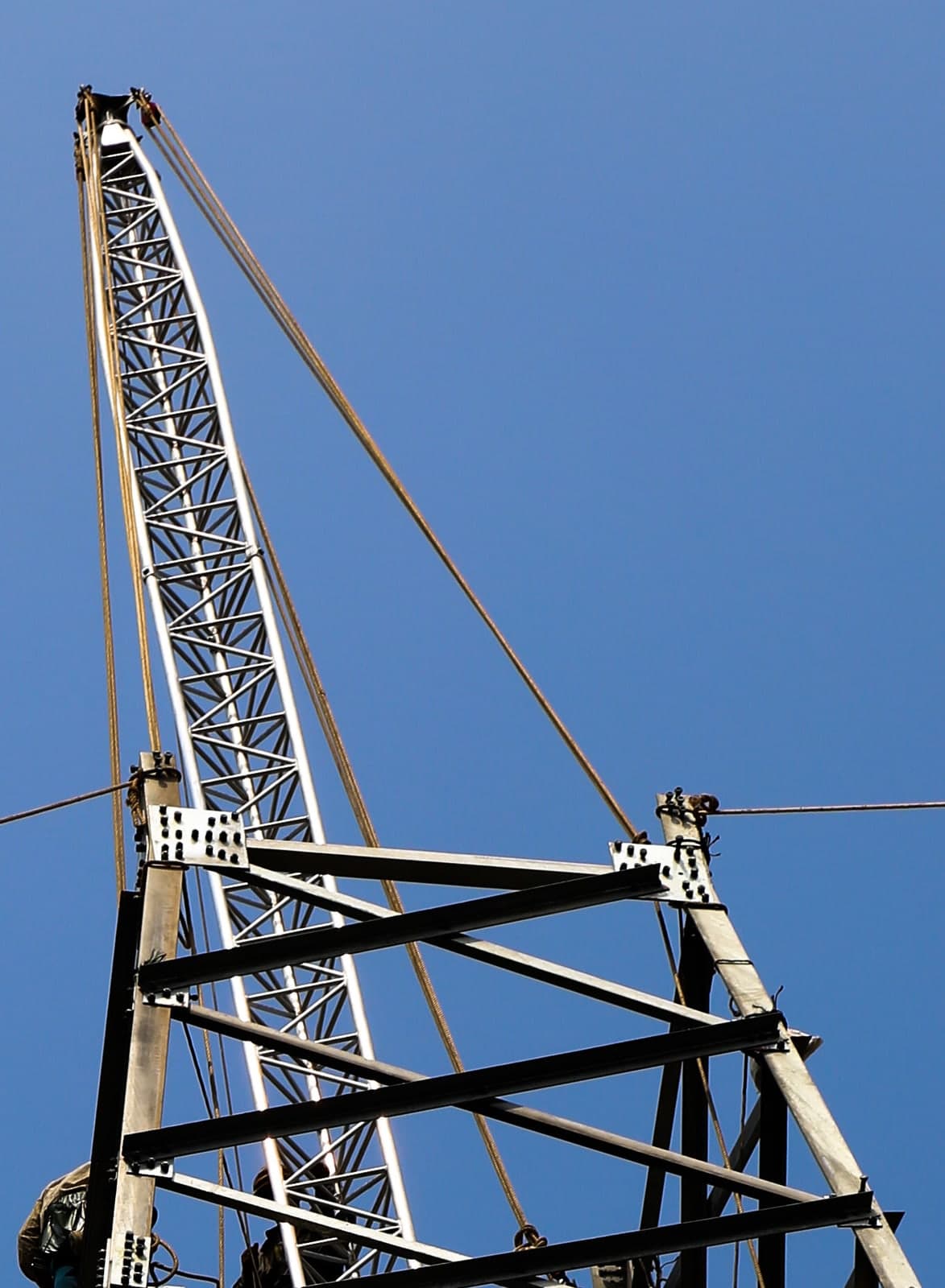 Gin pole during tower erection on a lattice tower against a blue sky